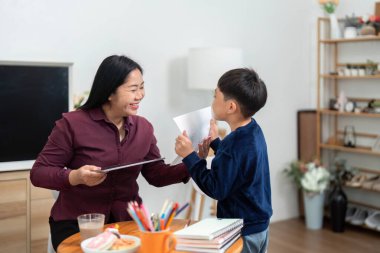 Genç bir çocuk gururla gülümseyen annesine sanat eserlerini gösterir. Okul yılına hazırlanırken bir neşe ve cesaret anı yakalar..
