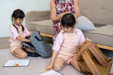 İki genç kız okul çantalarını ve sanat malzemelerini düzenlemekle meşguller. Gelecek okul yılının neşesini ve beklentilerini sergiliyorlar..