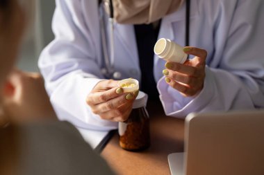 Bir sağlık hizmeti sağlayıcısı, bir hastaya ilaç şişesinin kullanımını açıklayan bir gösteri sunar. Bu etkileşim, tedavi yönetimi ve hasta eğitimini vurgulamaktadır.