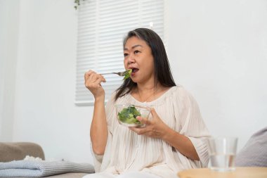 Bir kadın taze yeşilliklerle dolu canlı bir salatadan hoşlanır. Sağlıklı yaşama bağlılığını ve dengeli bir yaşam tarzını yansıtır..