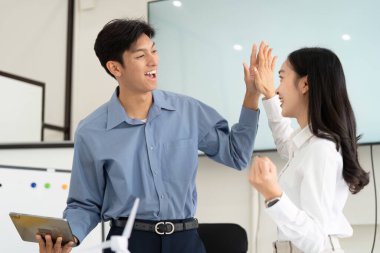 Genç bir erkek ve kadın, sürdürülebilirlik odaklı bir projede takım çalışmasının ve başarının altını çizerek modern bir ofiste bir kutlama anını paylaşıyor..