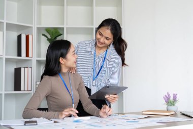 Proje detayları ve başarı stratejilerini tartışmak için modern bir çalışma alanında işbirliği yapan iki iş kadını, takım çalışmasını ön plana çıkarıyor.