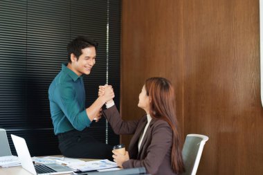 Uyumlu bir ofis ortamında, meslektaşlar takım çalışmasını ve ortaklığı sembolize ederek ortak başarılarını kutlamak için el sıkışırlar..