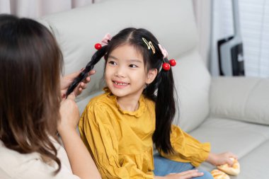 Bir anne kızına nazikçe saçını örer, sevgi dolu bağlarını gösterir ve sıcak bir atmosferde aile hayatının besleyici yönlerini gösterir..