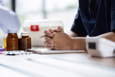 Bir sağlık uzmanı, tedavi ve tıbbi malzemeler etrafını sarmışken hasta bakımını tartışmaya hazır elleri kelepçeli bir şekilde toplantı masasında oturur..
