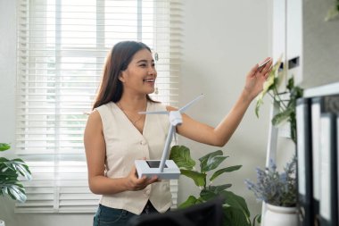 Parlak bir ofiste rüzgar türbini modeli sunan bir kadın sürdürülebilir enerji çözümleri ve kurumsal sorumluluğa olan bağlılığını yansıtıyor..