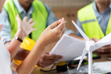 Rüzgar türbini projeleri için planlar ve modellerle beyin fırtınası yapan mühendisler, yeşil teknolojiye ve sürdürülebilir uygulamalara olan bağlılıklarını vurguluyorlar.
