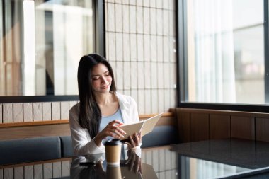 İçerik sahibi bir kadın en sevdiği kafede bir kitap okur, kahvesini yudumlarken rahatlamanın tadını çıkarır. Bu resim, sıcak bir ortamda geçirilen kişisel zamanın keyfini vurgular..