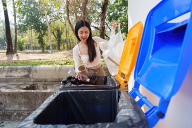 Neşeli bir kadın, çoklu geri dönüşümlü ürünleri atarak atık yönetimine aktif olarak katılıyor. Çevre yönetiminin ve sorumlu imha sisteminin önemini vurguluyor..