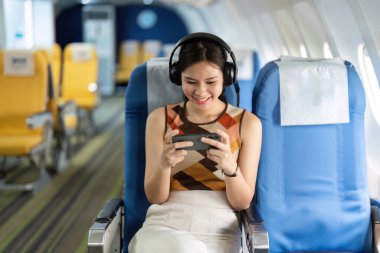 Uçaktaki neşeli bir turist, onun cihazına kendini kaptırmış durumda. Uçuşunda eğleniyor, bir anlık neşe sergiliyor..