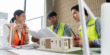 Çeşitli mühendislerden oluşan bir ekip, sürdürülebilir yapı planlarını ve modelleri parlak, modern bir ofiste inceleyerek yeşil teknoloji girişimleri üzerinde işbirliği yapıyor..