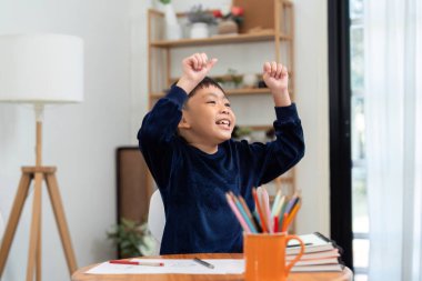 Evde bir görevi tamamladıktan sonra, eğitimde başarı ve motivasyonun önemini vurgulayan genç bir çocuk sevinç ve heyecan ifade ediyor..