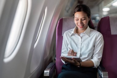 Profesyonel bir kadın iş seyahati deneyimine dalmış, uçuşunun keyfini çıkarırken not defterine not alarak mutlu bir şekilde not alır..