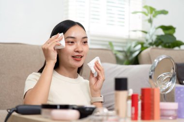 Bir kadın makyaj malzemelerini temizlemek için temizleme bezi kullanırken, rahat bir ortamda cilt bakımını sergilerken görülüyor. Görüntü kişisel bakım ve güzellik hazırlığını vurguluyor..