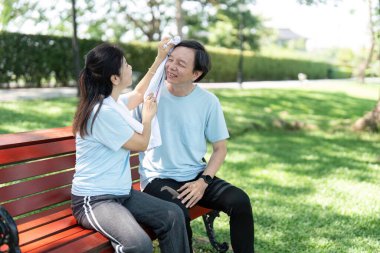 Ferahlatıcı bir yürüyüşten sonra, kıdemli bir çift bir bankta dinlenmek, havluyu ve kahkahayı paylaşmak, arkadaşlığın ve sağlığın sevincini vurgulamak için ara verir..