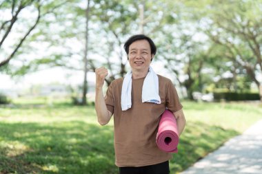 Yoga minderini gururla gösteren ve kararlılığını ifade eden mutlu bir son sınıf öğrencisi, canlı bir açık hava ortamında sağlık seansına hazır..