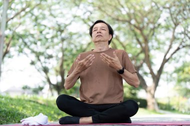 Dışarıda meditasyon yapan kıdemli bir adam, sakin bir ortamda sağlığını kucaklarken nefes alıp verişine ve farkındalığına odaklanıyor..