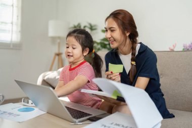 Neşeli bir anne kızına dizüstü bilgisayardaki görevlerinde yardım eder, evde eğitim ve bağ kurmayı teşvik eder..