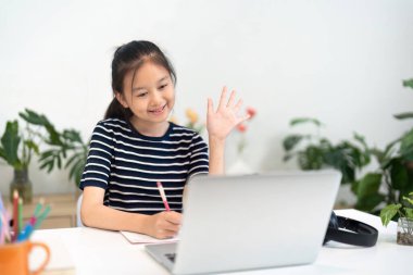 Genç bir kız çevrimiçi bir derse katılıyor, öğretmenine gülümsüyor ve el sallıyor, okula dönüş öğrenme ruhunu somutlaştırıyor..