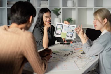 Ekibe mobil uygulama prototipleri içeren UX UI kavramlarını gösteren bir tasarımcı, parlak bir ofis alanında ilgi çekici bir tartışmayı kolaylaştırıyor.