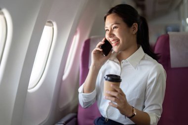 Neşeli bir iş kadını kahve yudumlarken, iş seyahatleri sırasında iş ve eğlence karışımını gösterirken telefonuyla konuşur..