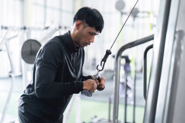 Kararlı bir genç, spor salonundaki fitness hedeflerine odaklanarak bir kablo makinesinde güç çalışması yapıyor..