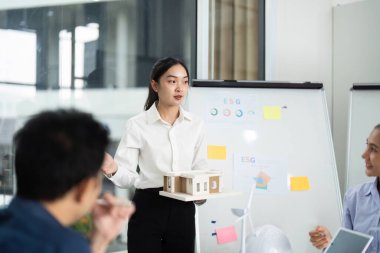 Bir mimar, işbirlikçi bir ofis ortamında ESG ilkelerini tartışırken, sürdürülebilirliği vurgulayarak bir model sergiliyor.