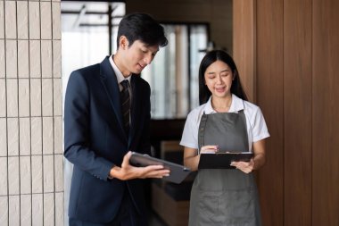 Bir ofis ortamında fikir alışverişinde bulunan ve belgeleri inceleyen iki genç profesyonel, takım çalışması ve işbirliği sergiliyor.