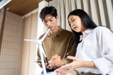 Yenilenebilir enerji stratejilerine odaklanan iki profesyonel, modern bir ofiste takım çalışması ve sürdürülebilirliğe olan bağlılıklarını gösteriyor.