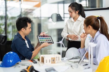 Erkek bir mühendis, iş arkadaşlarıyla sürdürülebilir mimariyi tartışırken proje verilerini gözden geçirir.