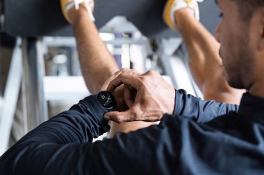 Bir kişi spor yaparken, spor yaparken, spor yaparken ve sağlık teknolojisini vurgularken, bir akıllı kasetteki uygunluk ölçümlerini izler..