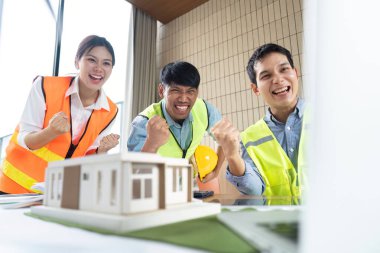 Üç mühendis sürdürülebilir bir inşaat modelinin tamamlanışını sevinçle kutluyor, takım çalışması ve başarı sergileniyor..