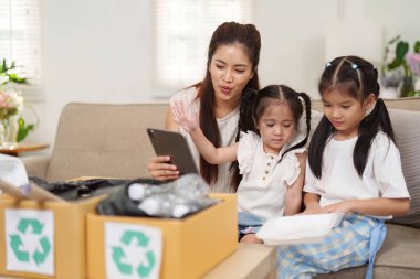 Bir anne ve iki kızı, geri dönüşümlü materyalleri sınıflandırırken sürdürülebilir uygulamaları araştırıyor, çocuklara çevreyi korumanın önemini öğretiyorlar..