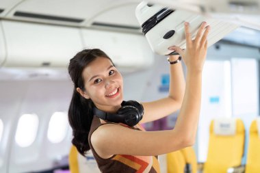 Bir uçuşta neşeli bir gezgin, gülümseyerek çantasını başınızın üstündeki bölmeye yerleştirir, yolculuğun heyecanını somutlaştırır..