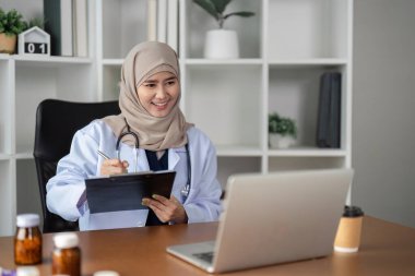 Başörtüsü takan neşeli bir kadın doktor, modern sağlık hizmetleri ve kapsayıcılığı vurgulayarak sanal bir konsültasyona girişiyor..