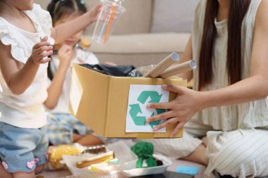 Bir anne, çocuklarına geri dönüşümlü materyalleri ayırmada rehberlik eder ve evde geri dönüşümün ve sorumlu atık yönetiminin önemini vurgular.