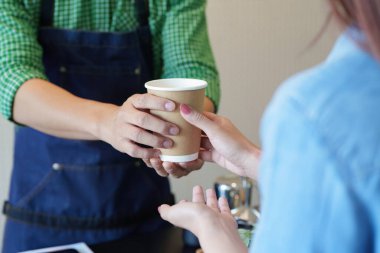 Modern bir kafede, bir barista çevresel bilinç ve müşteri bakımını vurgulayarak sürdürülebilir bir fincanda hazır kahve sunar..