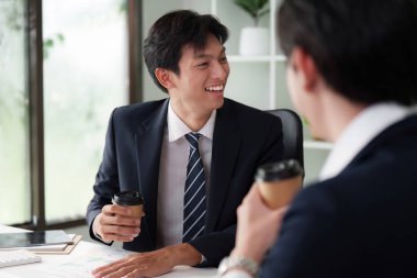 Genç bir profesyonel, iş arkadaşlarıyla canlı bir ofiste kahve içerek, fikir alışverişinde bulunur ve yaratıcı ve yenilikçi bir çalışma ortamı oluşturur..