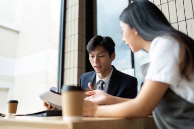 İki profesyonel, çağdaş bir kafe ortamında kahve içerken proje planları hakkında bir tartışmaya girişirken, takım çalışmasını ön plana çıkarıyorlar..