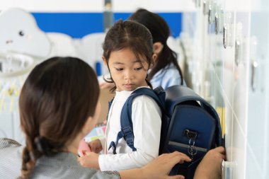 Genç bir kız okul için hazırlanıyor, annesi ona dolaplarda yardım ederken sırt çantasını ayarlıyor. Bir bağlantı ve destek anı.