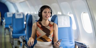 Uçaktaki neşeli bir gezgin, kulaklıklar ve akıllı telefonuyla yolculuğunun tadını çıkarıyor, modern seyahat tarzının vücut bulmuş hali..