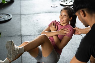 Bir bayan müşteri temel egzersizleri yaparken, kişisel antrenör fitness stüdyosunda cesaret ve rehberlik sunar..