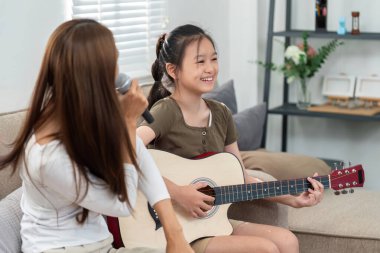 Annesi şarkı söylerken gitar çalan genç bir kız sıcak ve sevgi dolu bir ortam yaratıyor. Aile ve müzik temaları için mükemmel.