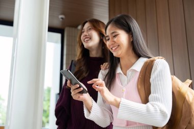 Şık bir akademik ortamda, her iki öğrenci de birbirlerini desteklerken aynı zamanda akıllı telefonlarıyla hevesle iletişim halindedirler..