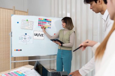 Profesyonel bir ortamda, bir kadın UX UI fikirlerini özetlerken meslektaşları yaratıcı beyin fırtınası sürecine girişiyor, işbirliği ve yenilikçi düşünce sergiliyor..