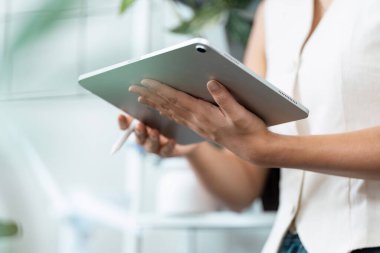 Bir kadın tabletiyle etkileşime girer, uygulamaları yönlendirmek için stil kullanır. Görüntü, teknolojinin günlük görevlere entegrasyonunu, üretkenliği ve modern çalışma kültürünü gözler önüne seriyor.