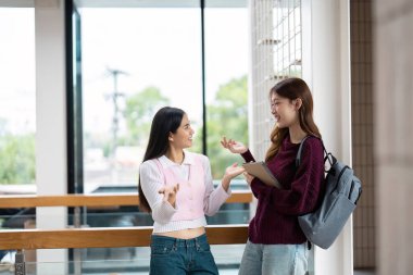 İki arkadaş hareketli bir şekilde sohbete dalıyorlar, eğitimsel bir ortamda ortak tartışmaların heyecanını yakalıyorlar, arkadaşlığın sıcaklığını vurguluyorlar..