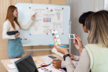 Odaklanmış bir atölyede, UX UI uzmanı, meslektaşlarının çalışmalarını inceleyerek, takım çalışmalarını ve yaratıcı sinerjiyi vurgulayarak hayati tasarım unsurlarını sergilemektedir..