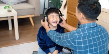 Baba, evdeki öğrenme deneyimini geliştirmek için oğluna kulaklıkla yardım ediyor. Paylaştıkları kahkahalar, okul yaklaştıkça birlikte öğrenmenin mutluluğunu simgeliyor..