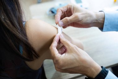 Bir klinikte hasta koluna aşı uygulayan bir tıp uzmanı, hasta bakımı ve aşı öneminin altını çiziyor..